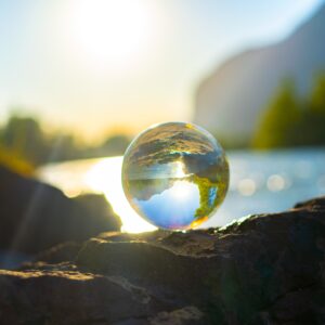 Glass ball reflecting light from sun and river in green landscape